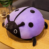 Colorful plush ladybug pillow in purple and black resting on a wooden table.
