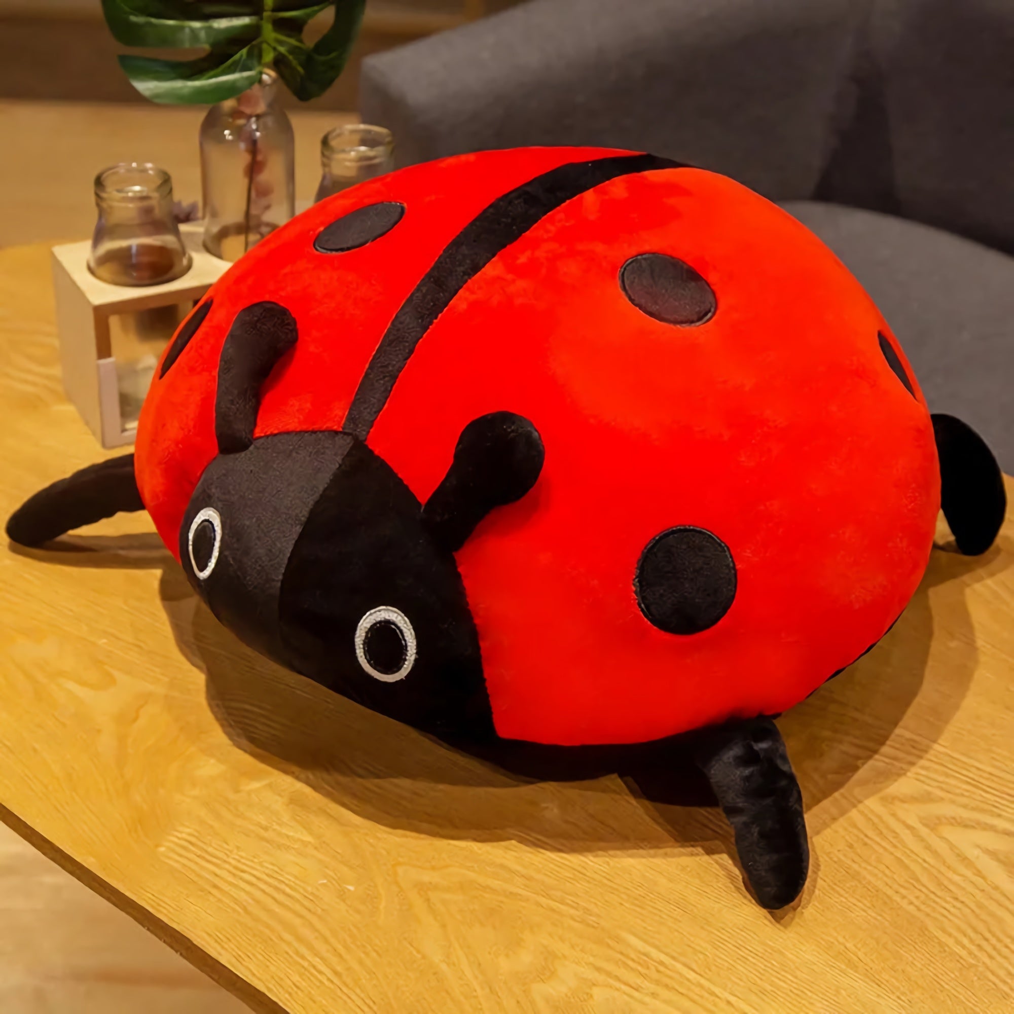 Colorful plush ladybug pillow with black spots and antennae, resting on a wooden table.