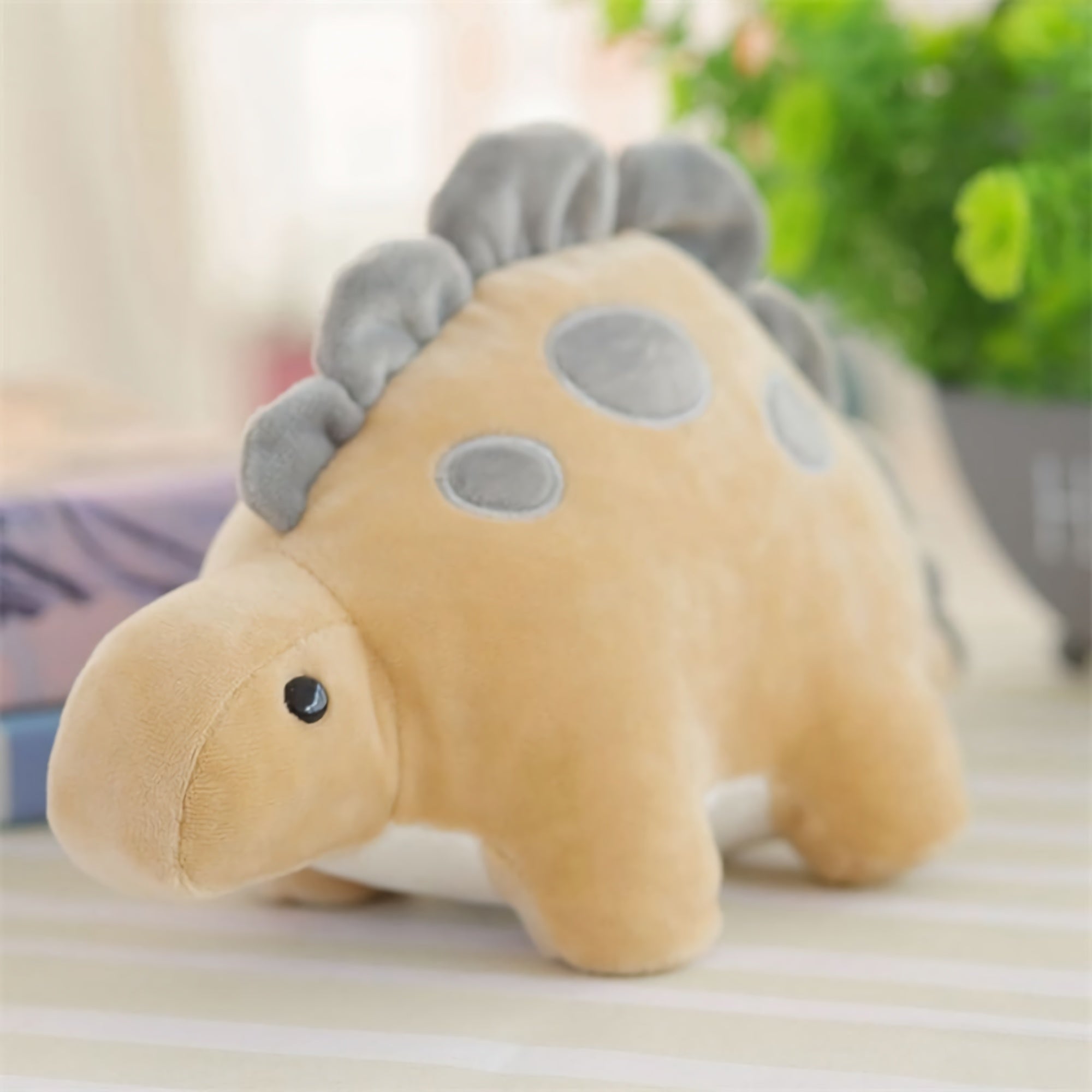 Pastel-colored dinosaur plush toy with gray spots and a soft texture, sitting on a striped surface.