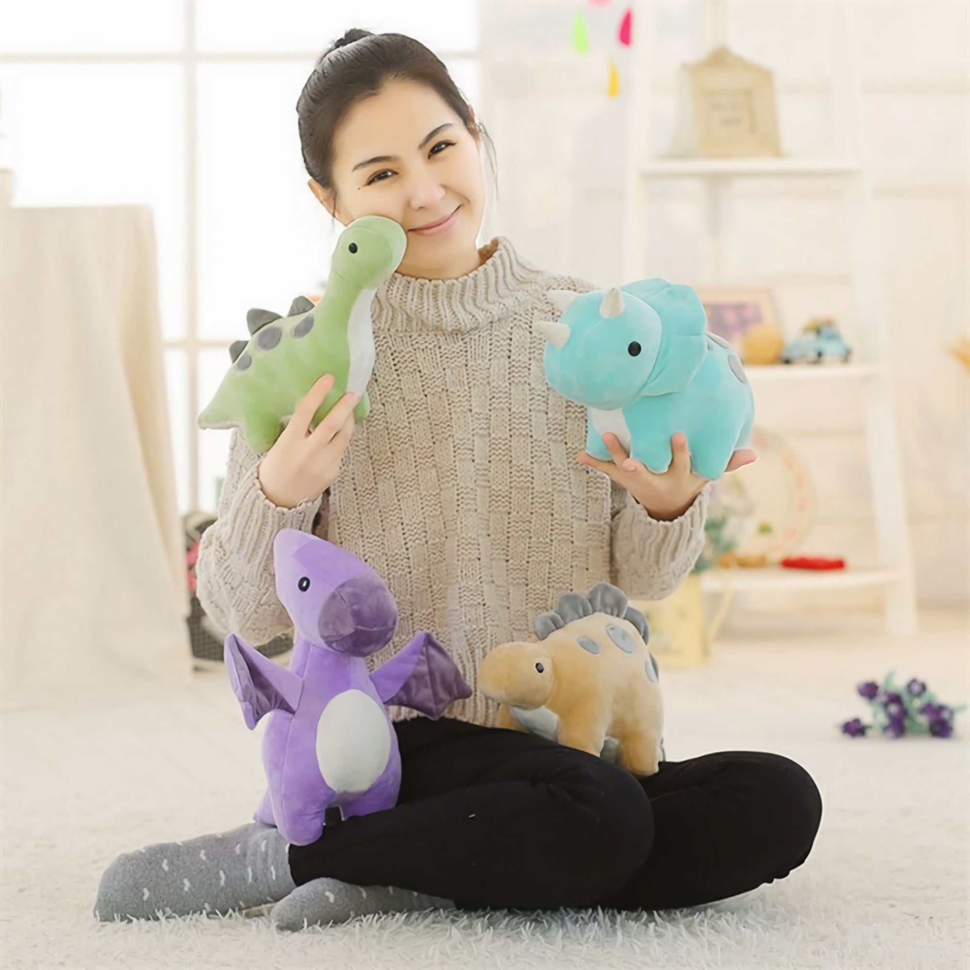 A person sitting on a rug holds four colorful dinosaur plush toys in a bright room.