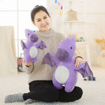A woman sits on the floor holding two purple dinosaur plush toys, smiling in a bright, cozy room.