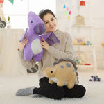 A person sits on the floor holding a purple dinosaur plush toy and a tan dinosaur plush toy beside them.