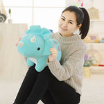 A person sitting on the floor holds a large, light blue dinosaur plush toy with a friendly expression.