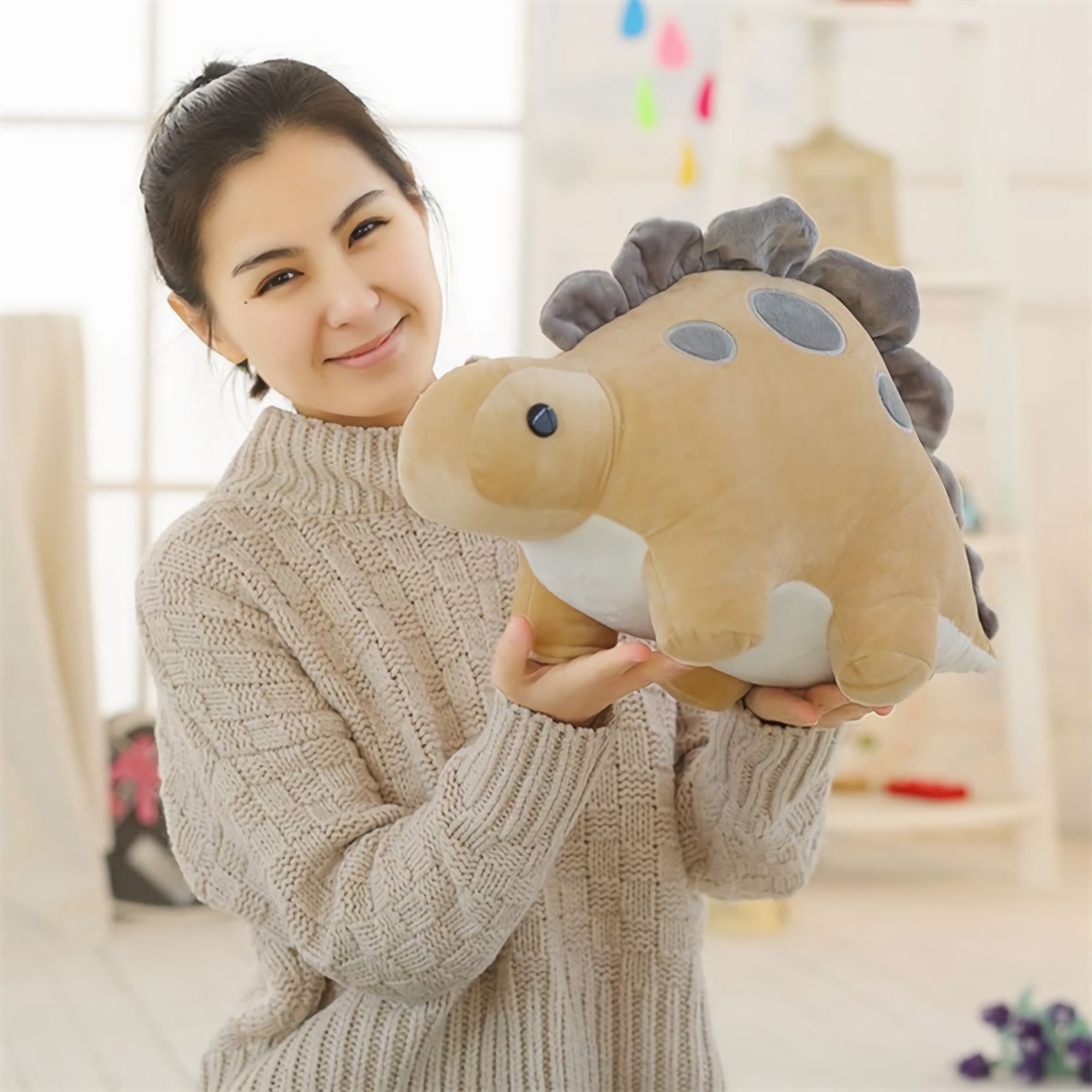 A woman in a sweater holds a large, soft, pastel-colored dinosaur plush toy.