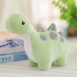 Pastel green dinosaur plush toy with gray spots and a white belly, sitting on a striped surface.