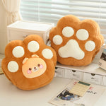 Two plush paw-shaped cushions in orange and white, featuring a cute animal face on one, placed on a table with a calculator.
