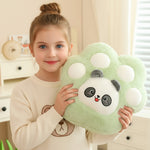 Girl holding a green plush paw-shaped pillow with a panda face, smiling in a cozy room.