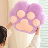 A person holds up a large, plush purple paw-shaped cushion with pink pads.