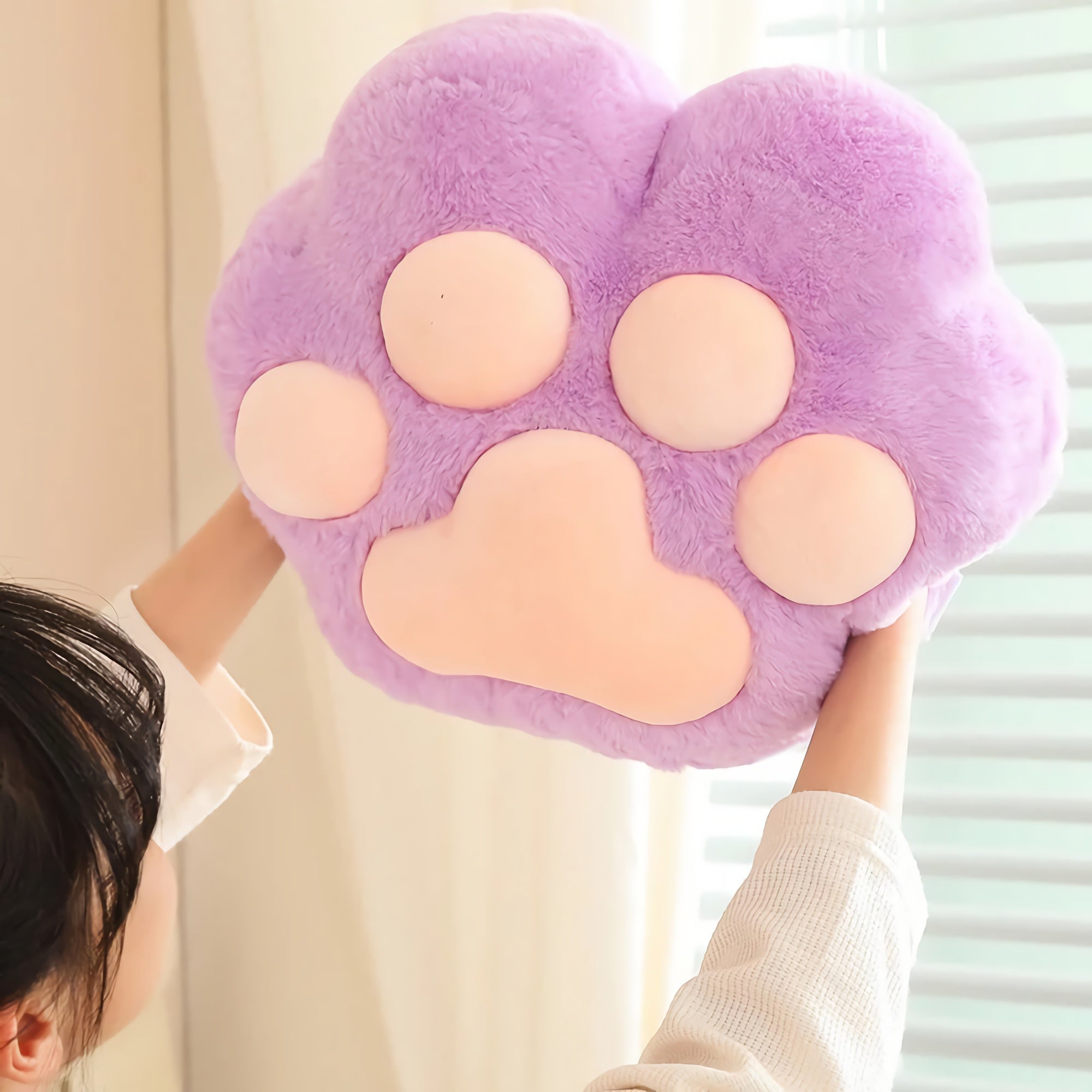 A person holds up a large, plush purple paw-shaped cushion with pink pads.