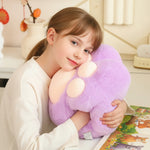 Child hugging a purple plush pillow shaped like a paw while sitting at a table.
