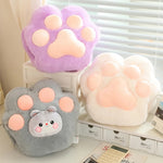 Three plush paw-shaped cushions in purple, gray, and white on a shelf.