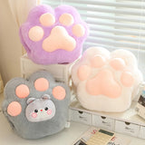 Three plush paw-shaped cushions in purple, gray, and white on a shelf.
