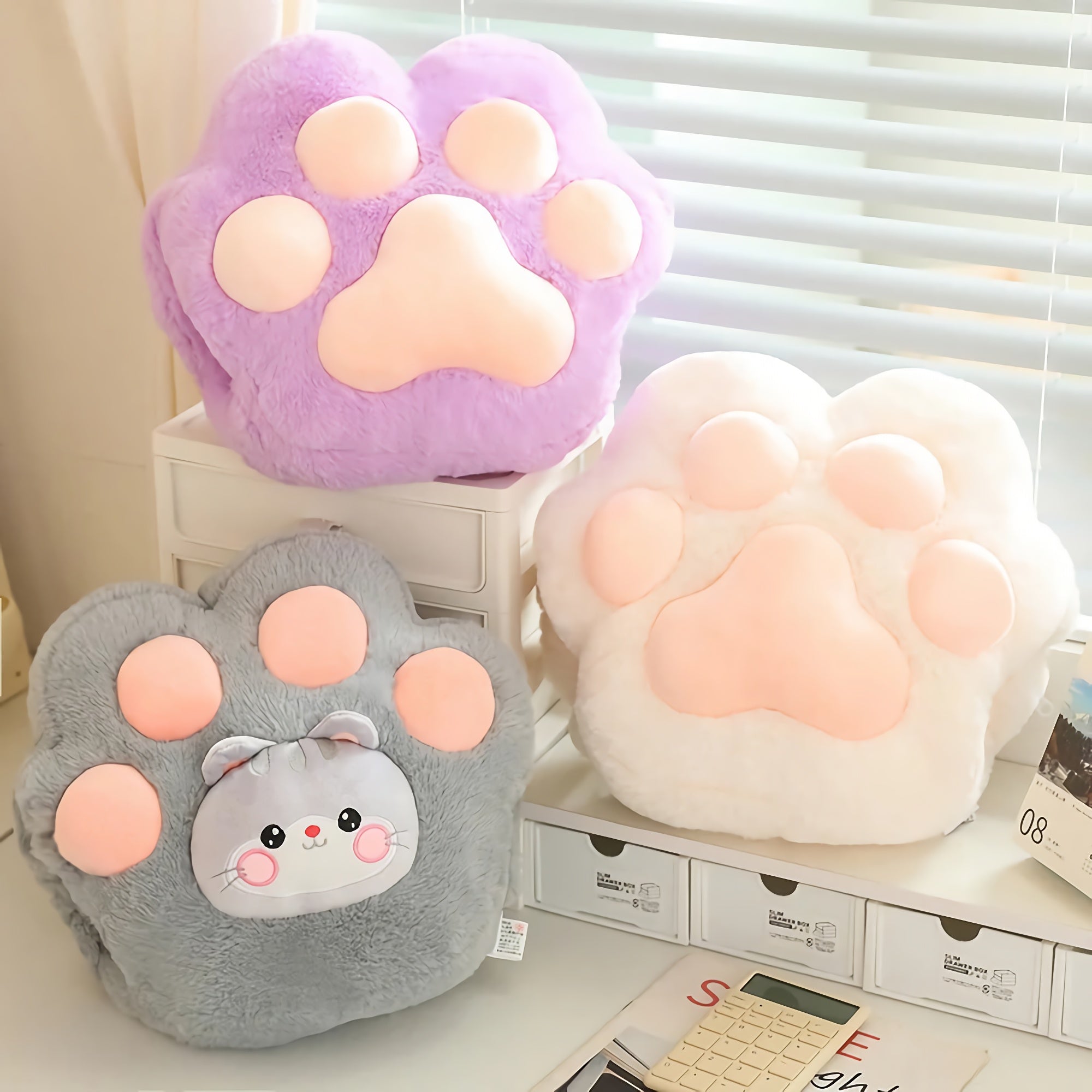 Three plush paw-shaped cushions in purple, gray, and white on a shelf.