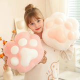 A girl holds two plush paw-shaped pillows, one pink and one white, smiling in a bright room.