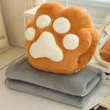 A plush orange paw-shaped pillow sits atop a folded gray blanket on a table.