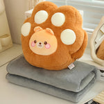 A plush paw-shaped pillow with a smiling face sits atop two folded gray blankets.