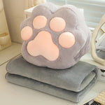 A gray plush blanket folded under a paw-shaped pillow with pink paw pads, placed on a light-colored surface.