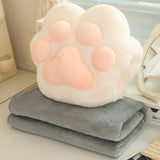Plush paw-shaped pillow on a folded gray blanket on a desk.