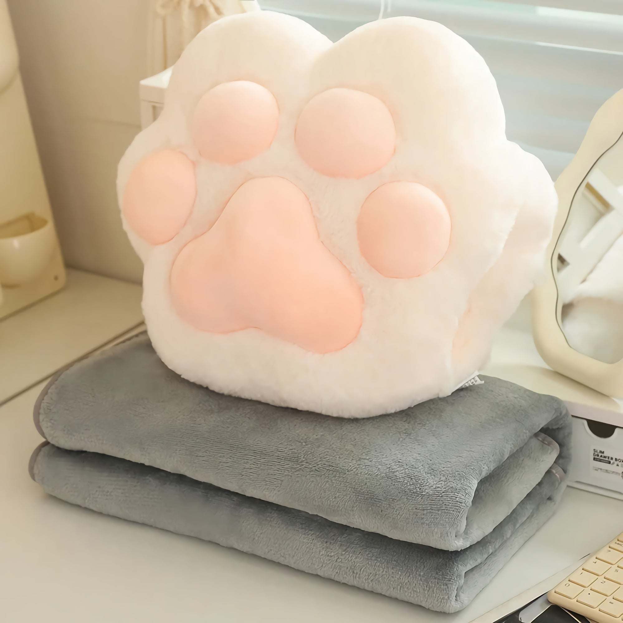 Plush paw-shaped pillow on a folded gray blanket on a desk.