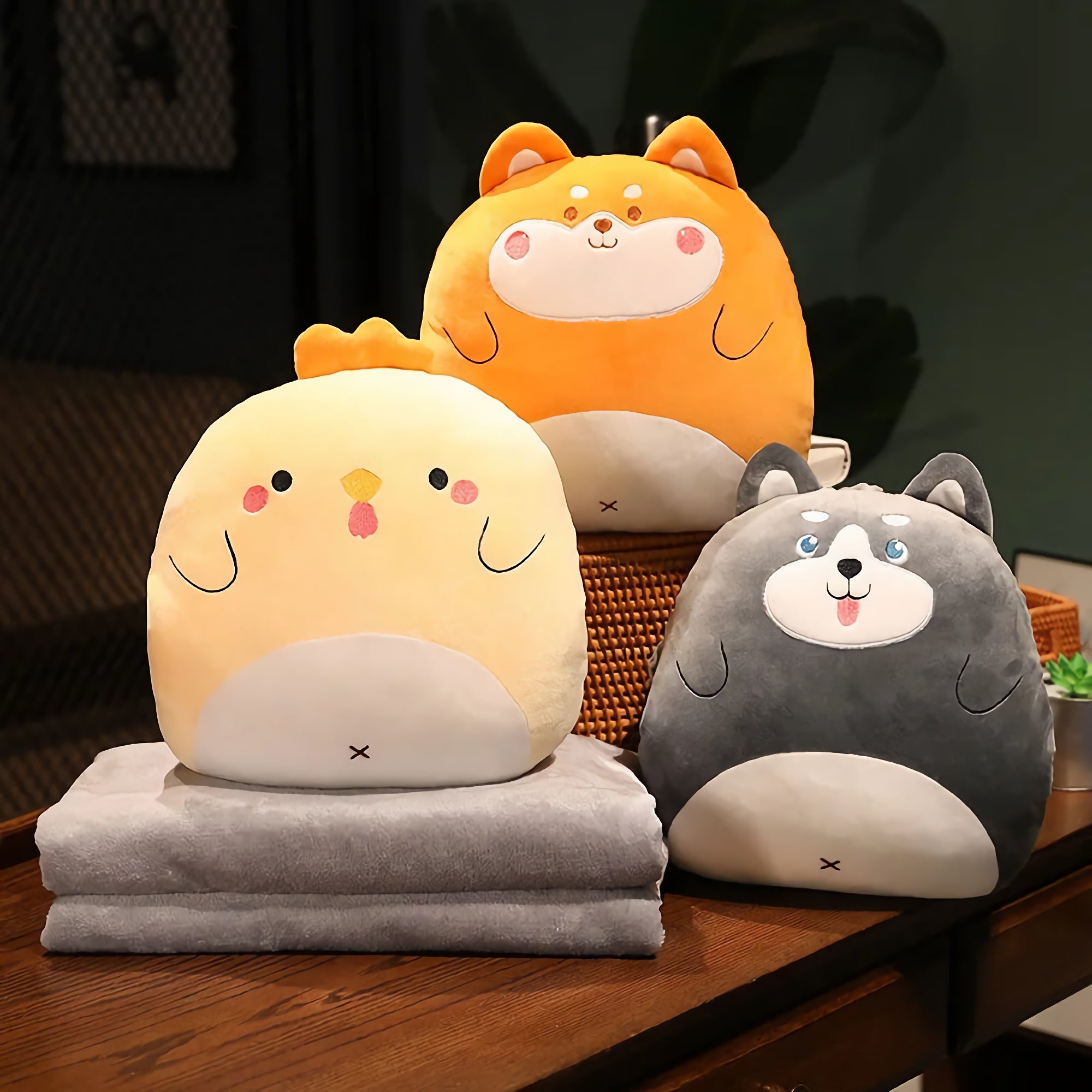Three plush animal pillows in yellow, orange, and gray, with two soft gray blankets stacked underneath.