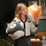 A girl holds two plush pillows shaped like animals, one gray and one orange, while smiling in a cozy room.