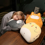Child sleeping on a table with three plush pillows shaped like animals, wrapped in a gray blanket.