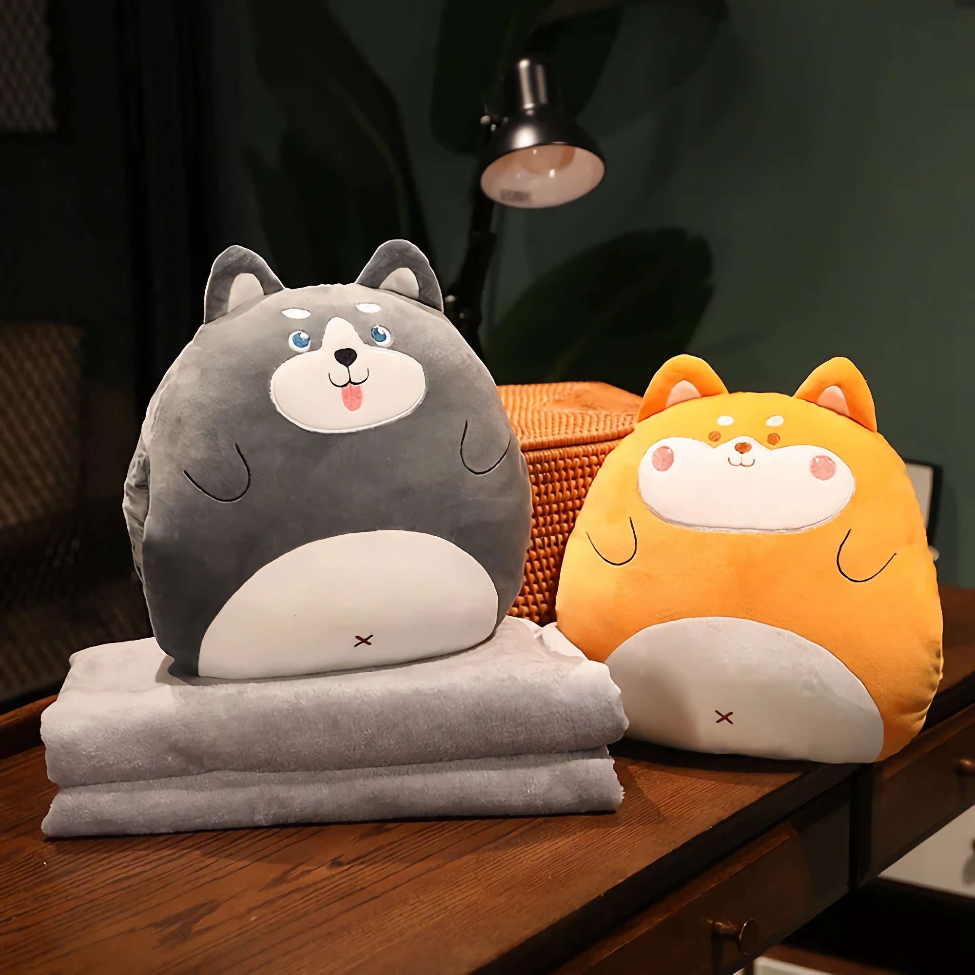 Two plush animal pillows, one gray and one orange, sit on a wooden table with folded gray blankets underneath.