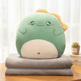 A green plush pillow shaped like a cute creature rests on two folded gray blankets.