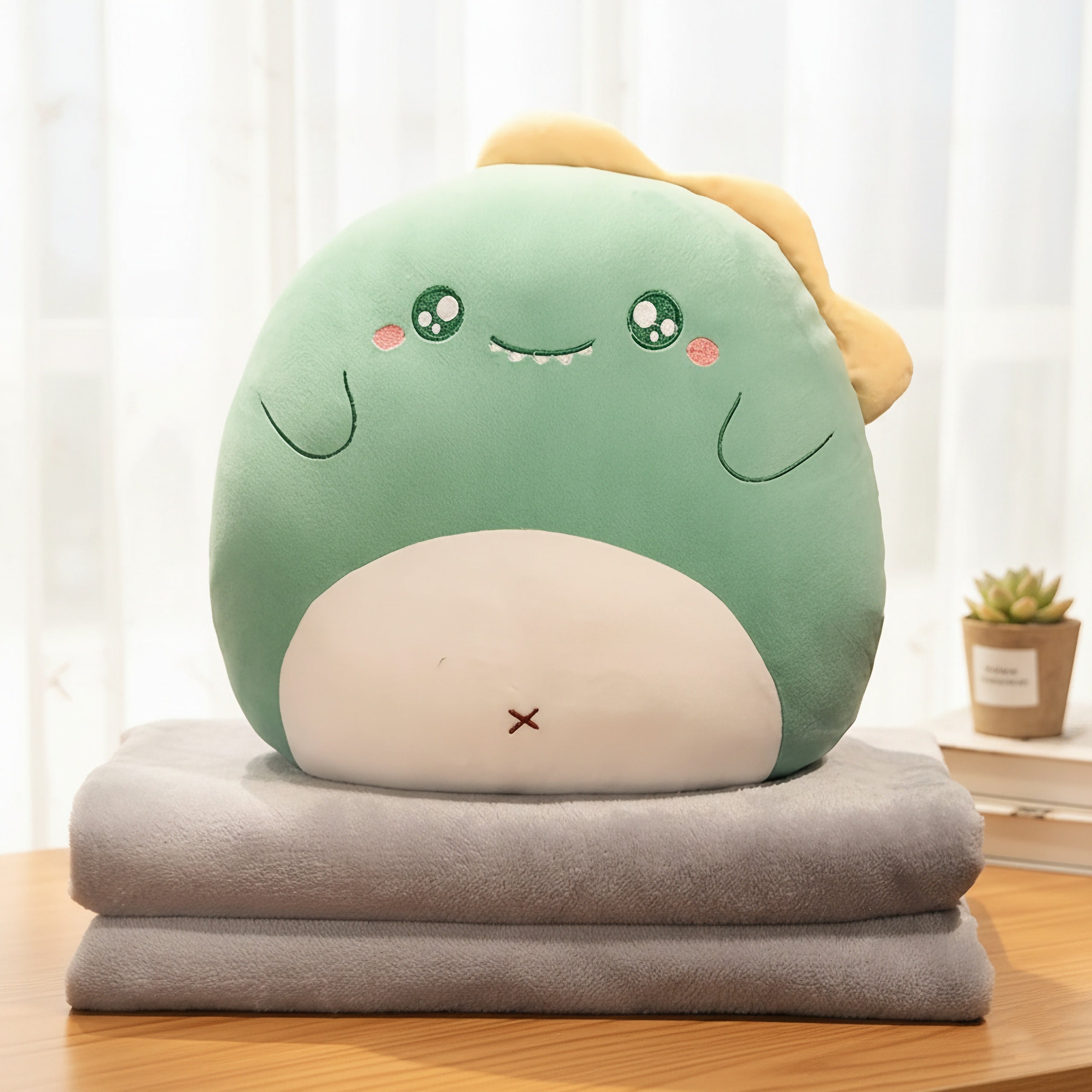 A green plush pillow shaped like a cute creature rests on two folded gray blankets.