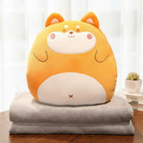 A plush orange animal pillow with a smiling face sits atop two gray blankets on a wooden table.
