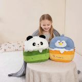 A girl smiles while holding two plush pillows shaped like a panda and a bird, sitting on a bed with a blanket.