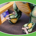 Close-up of a Spinosaurus plush toy's feet and legs, featuring green and yellow detailing, resting on a chair.