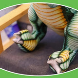 Close-up of a Spinosaurus plush toy's feet and legs, featuring green and yellow detailing, resting on a chair.