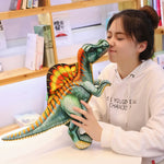 A person holds a colorful Spinosaurus plush pillow close to their face in a cozy indoor setting.