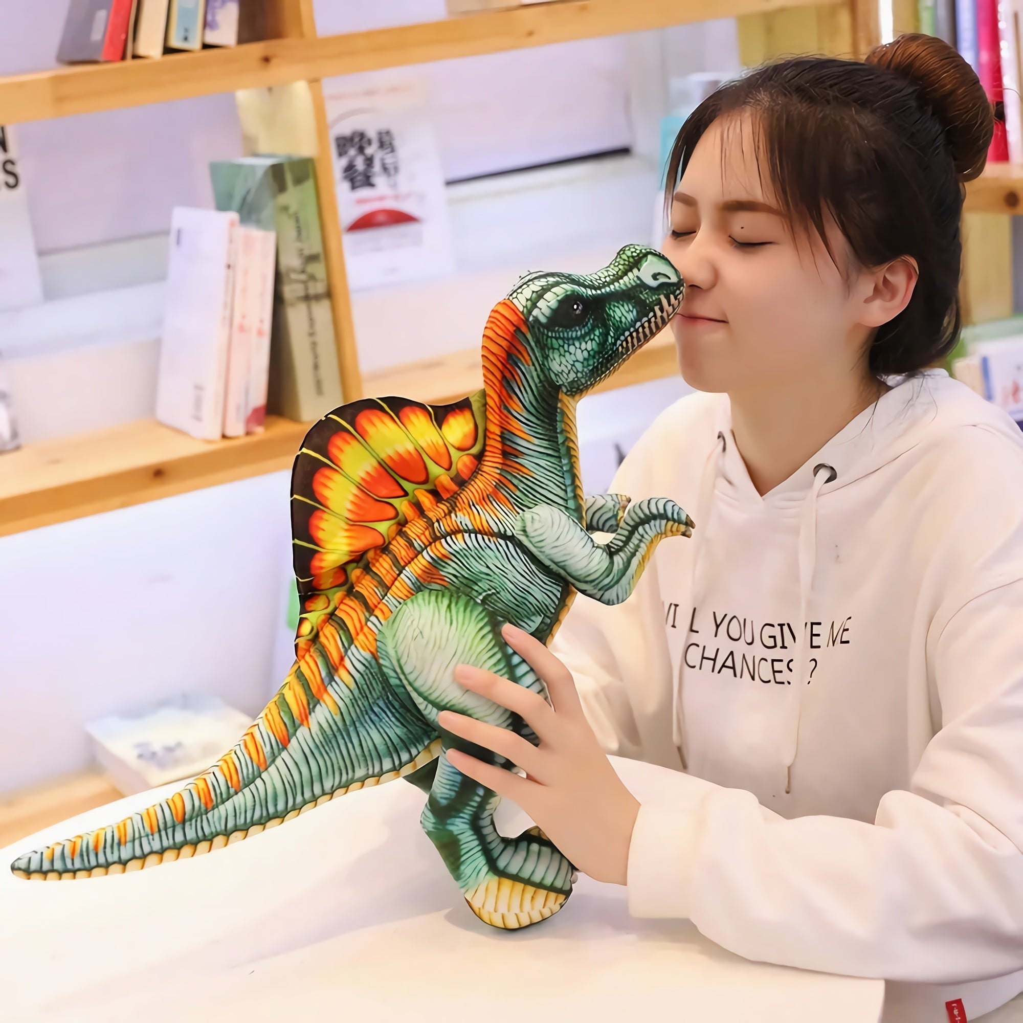 A person holds a colorful Spinosaurus plush pillow close to their face in a cozy indoor setting.