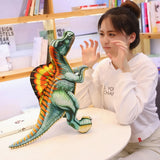A woman playfully interacts with a colorful Spinosaurus plush pillow on a table in a cozy setting.