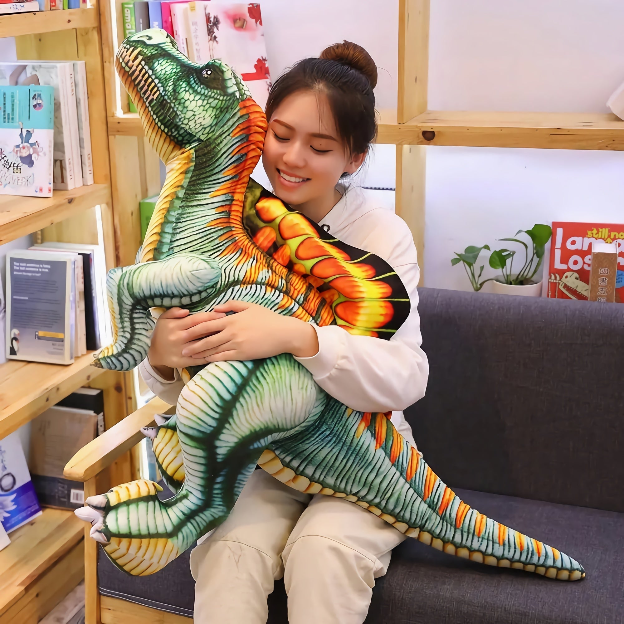 A person hugs a large, colorful Spinosaurus plush pillow while sitting on a couch in a cozy room.