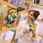 A person holds a small Spinosaurus plush toy while standing next to a larger one on a wooden shelf filled with books.