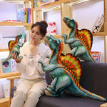 A person sits on a couch with colorful Spinosaurus plush toys, contemplating while holding one in their hand.